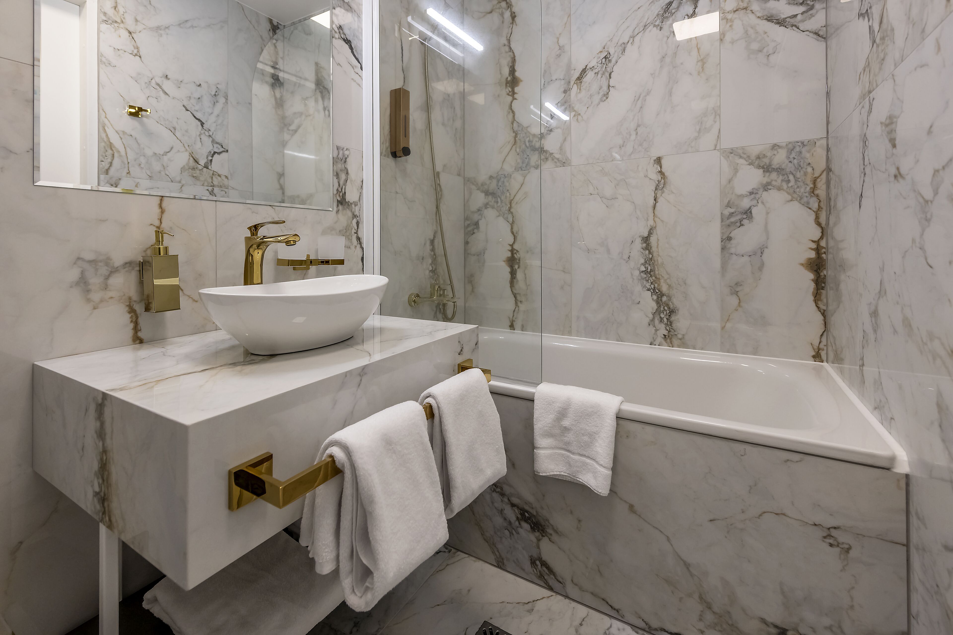 A bathroom with a white marble sink, gold fixtures, and a glass-enclosed shower.
