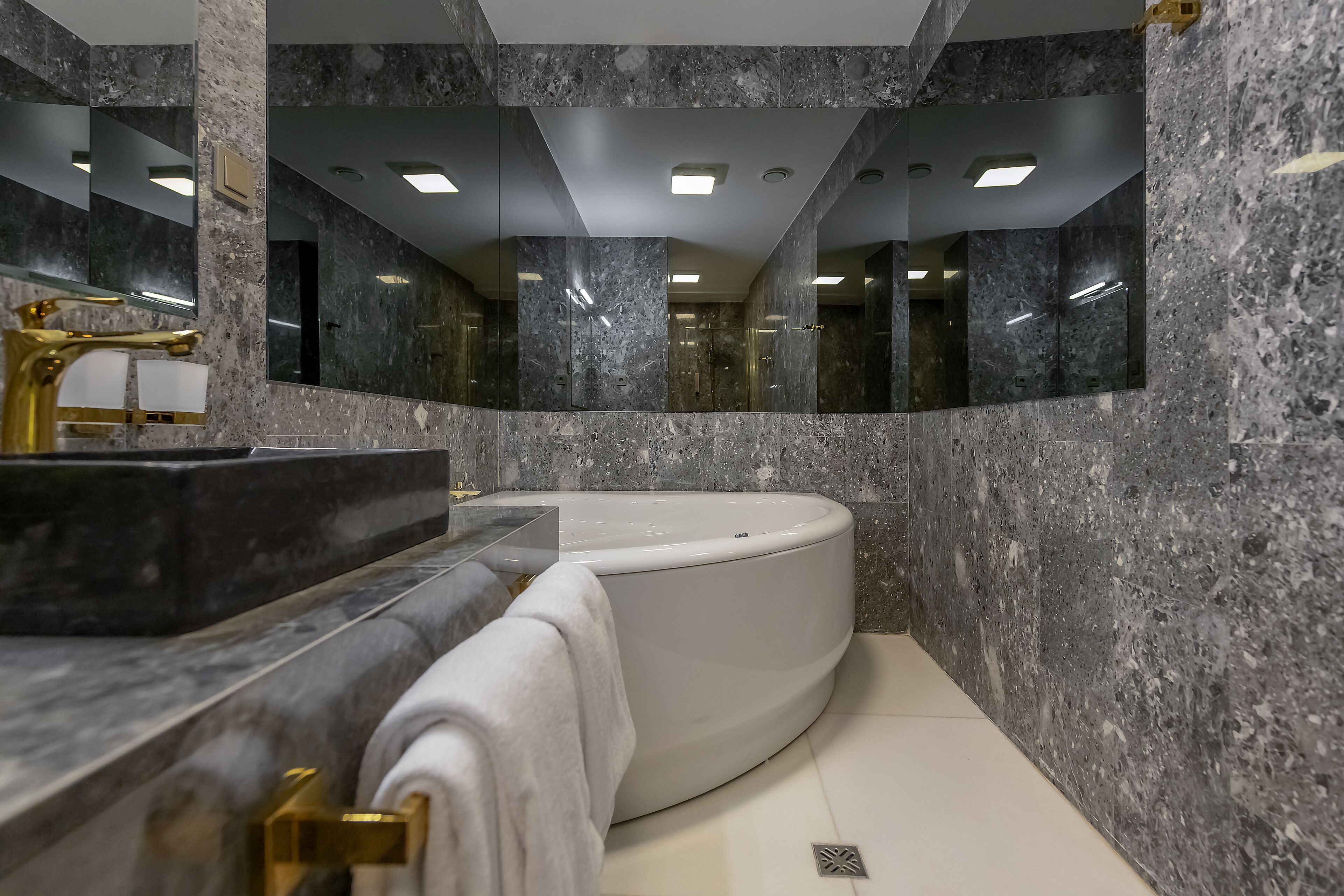 Une salle de bain moderne avec un mur en marbre, un grand miroir, une baignoire et un robinet doré.