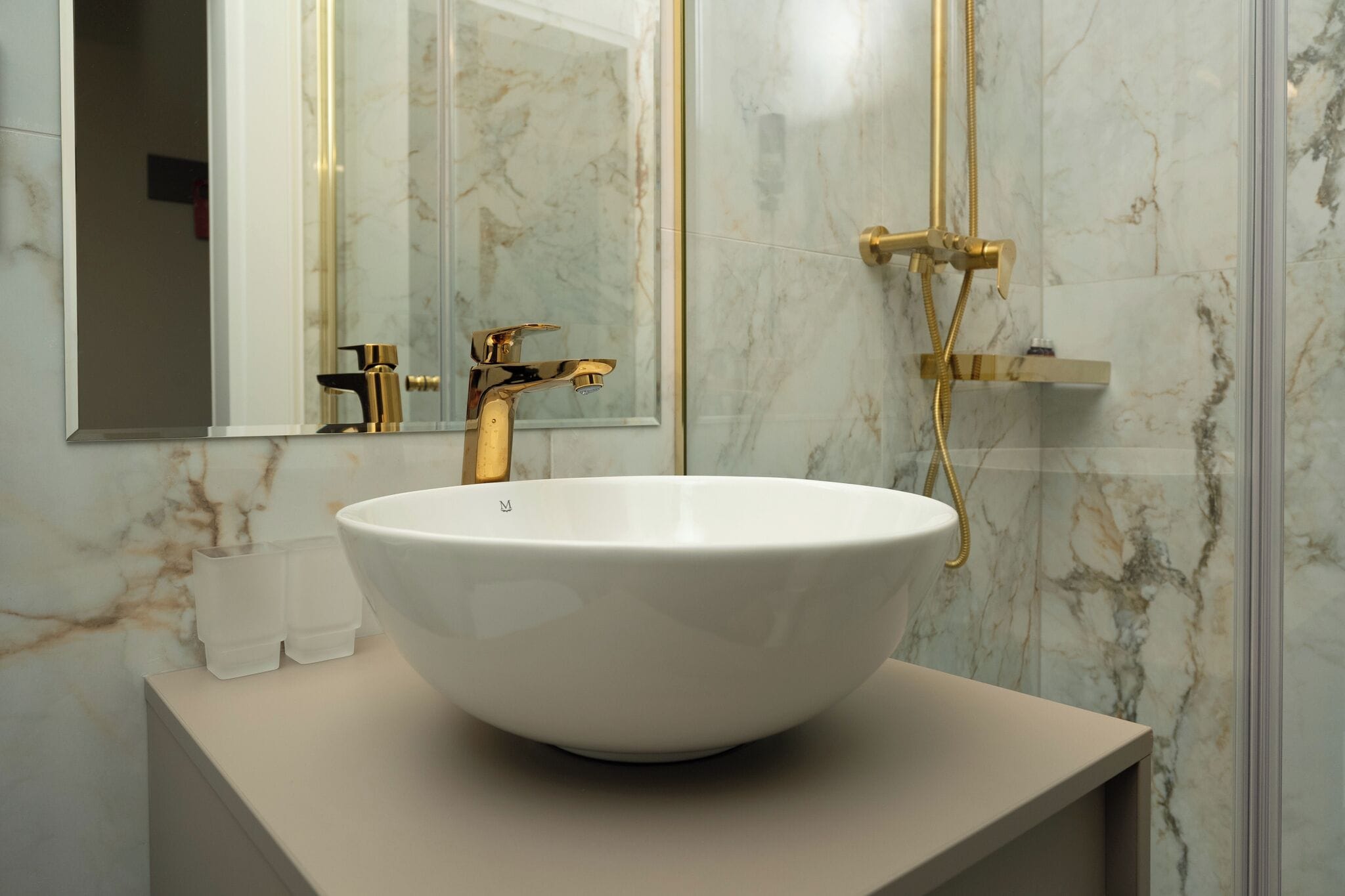 Een badkamer met een wit marmeren wastafel, gouden details en een douchecabine van glas.