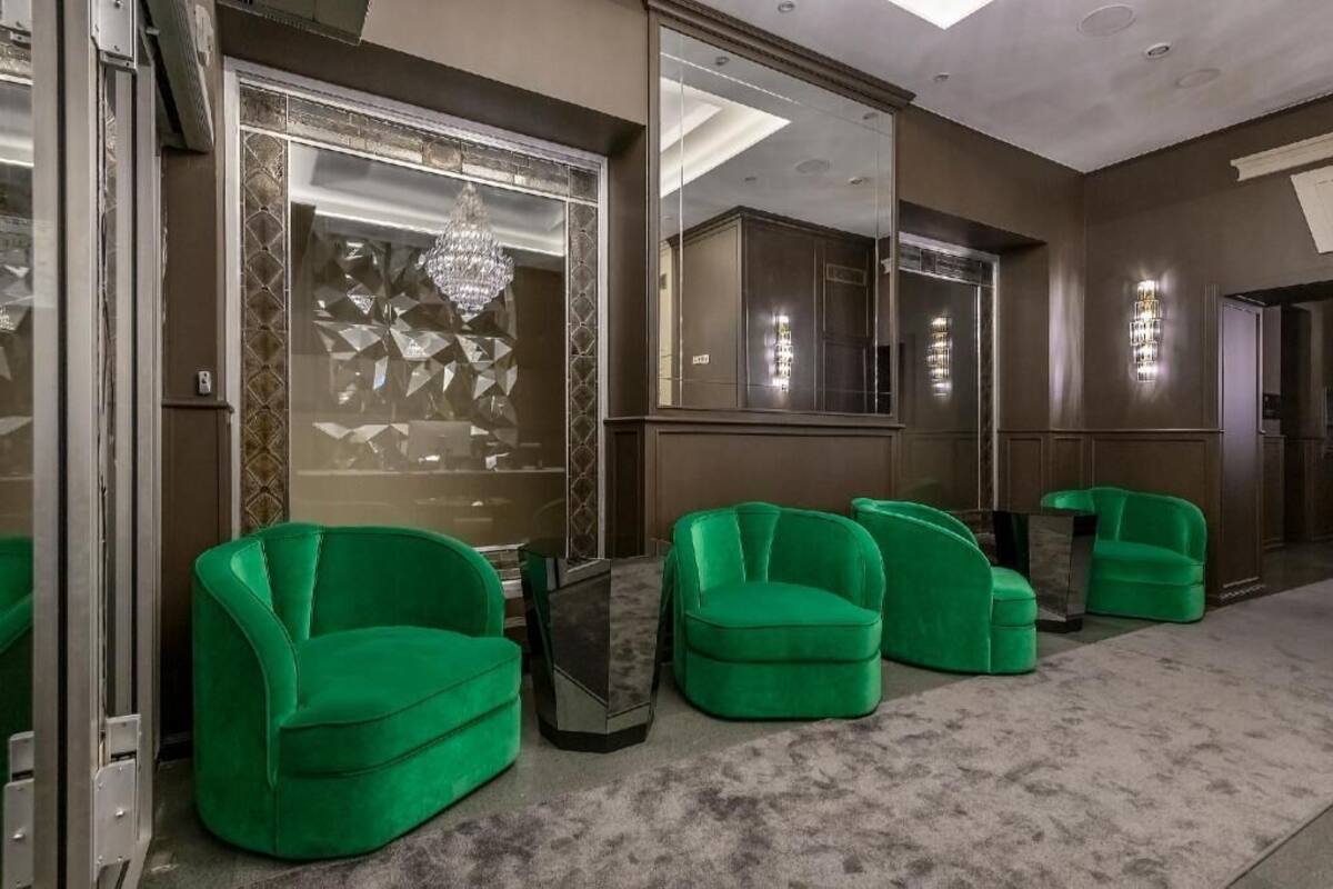 A hotel lobby with green armchairs, a large mirror, and a chandelier.