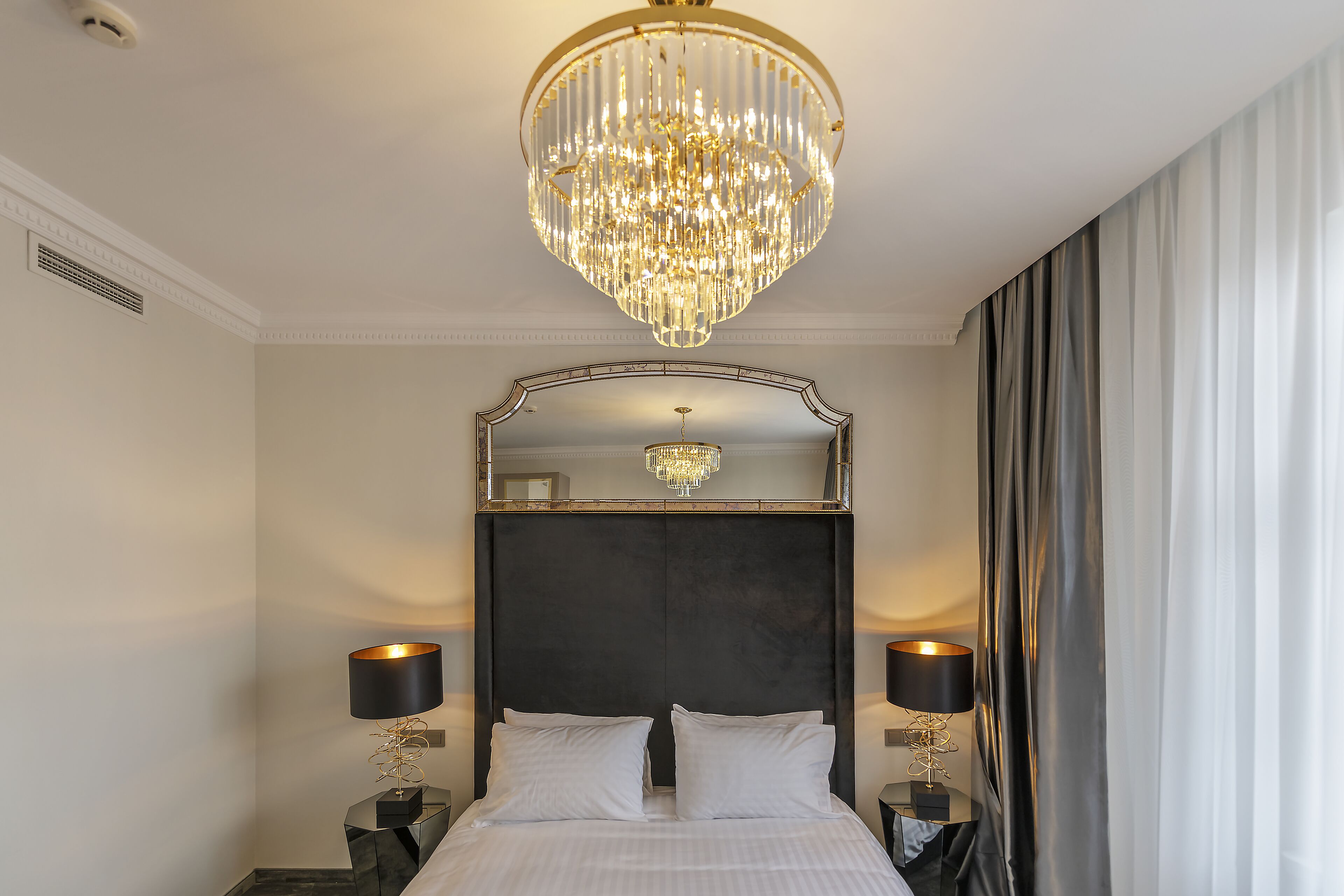 Ein Hotelzimmer mit einem großen Bett, zwei Nachttischen mit Lampen, einer Kristallleuchtre und einem Spiegel über dem Bett.
