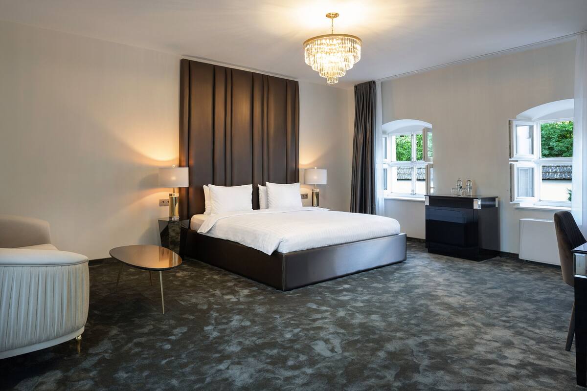 A modern hotel room with a large bed, a bedside table, a chair, and a desk.