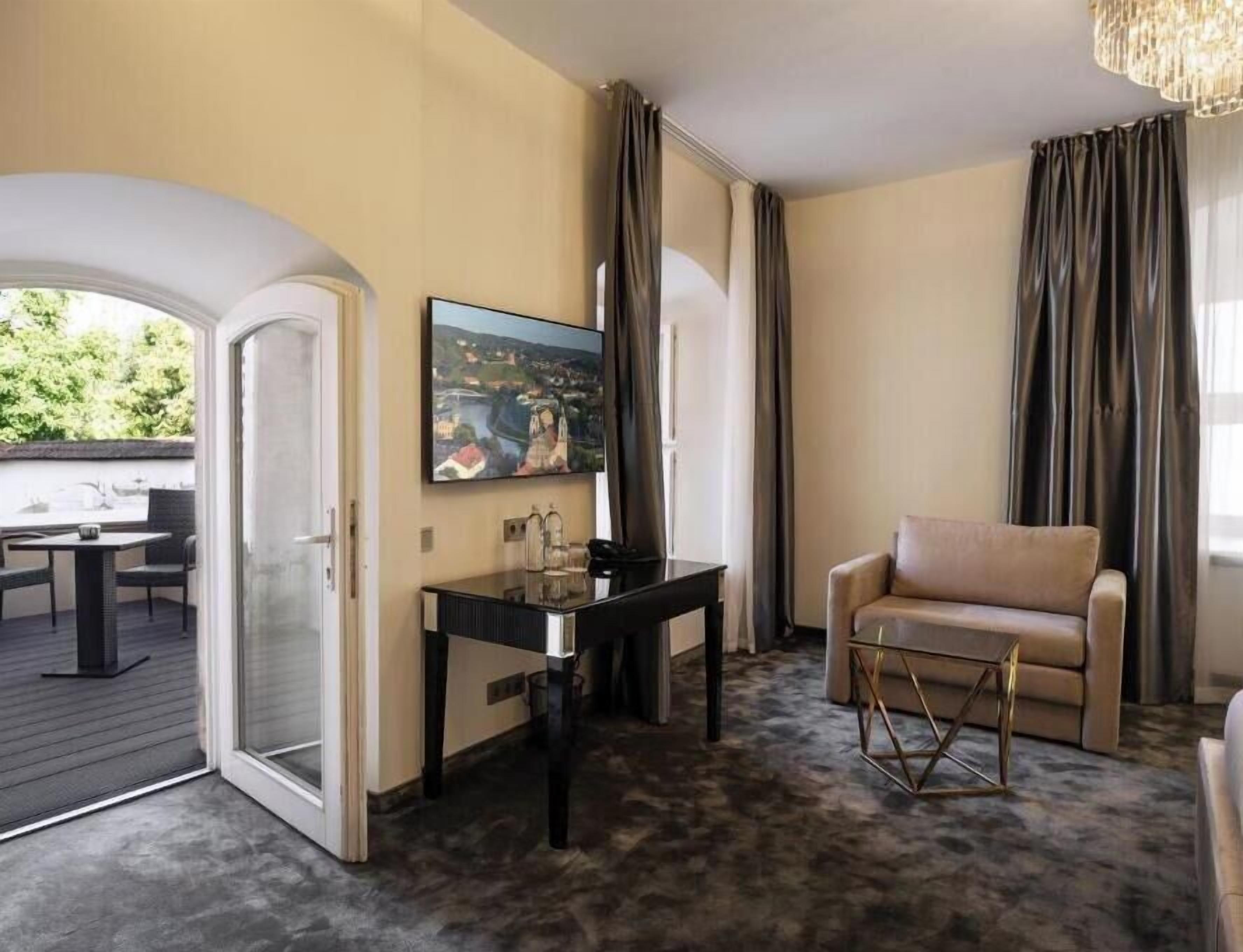 A hotel room with a dining area, a sofa, a TV, and a painting.
