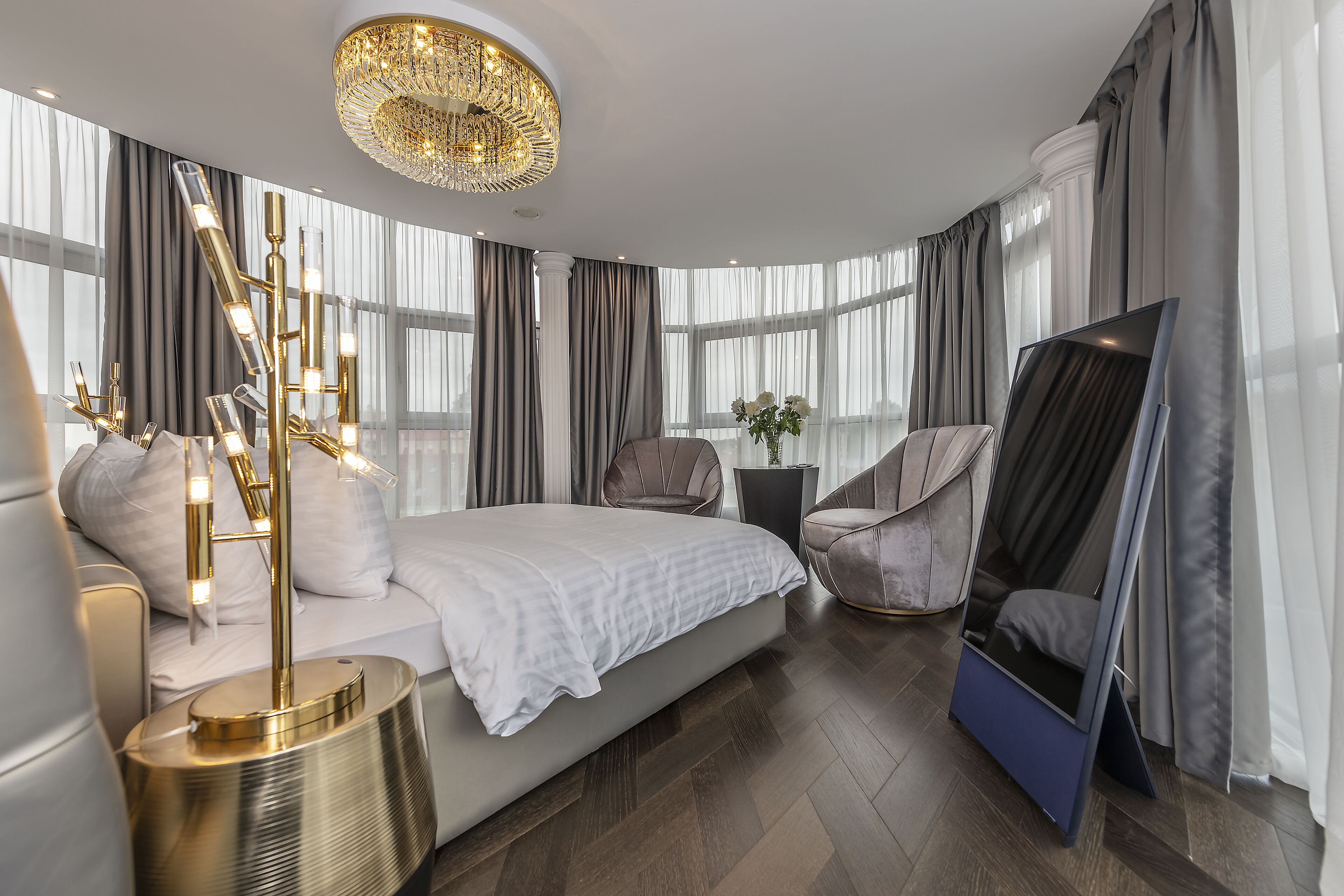 A modern bedroom with a large bed, a TV, a chair, and a decorative floor lamp.