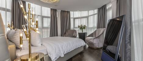 A modern bedroom with a large bed, a TV, a chair, and a decorative floor lamp.