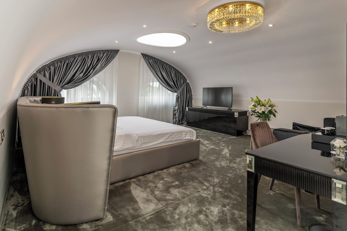 A modern hotel room with a curved ceiling, a large bed, a desk, and a television.