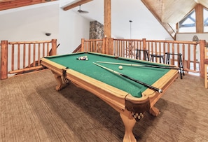 A pool table in a room with wooden railings and a stone wall.