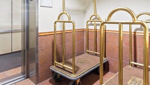 A hotel elevator with a closed door, a wall-mounted sign, and a luggage cart with wheels.