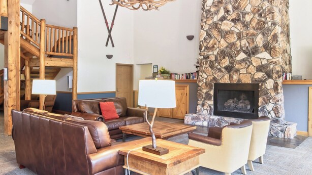 A spacious living area with a stone fireplace, leather sofas, and a wooden staircase.