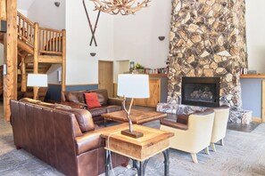 A spacious living area with a stone fireplace, leather sofas, and a wooden staircase. - Walk to Lift. Hot Tubs. Elevator. Close to Lake. (Keystone)