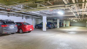 An underground parking garage with multiple cars parked, concrete pillars, and visible pipes on the ceiling.