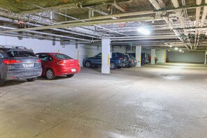 An underground parking garage with multiple cars parked, concrete pillars, and visible pipes on the ceiling.
