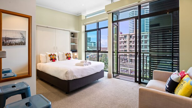 Una moderna camera d'hotel con un letto grande, un balcone vista città e una zona salotto con divano e poltrone.