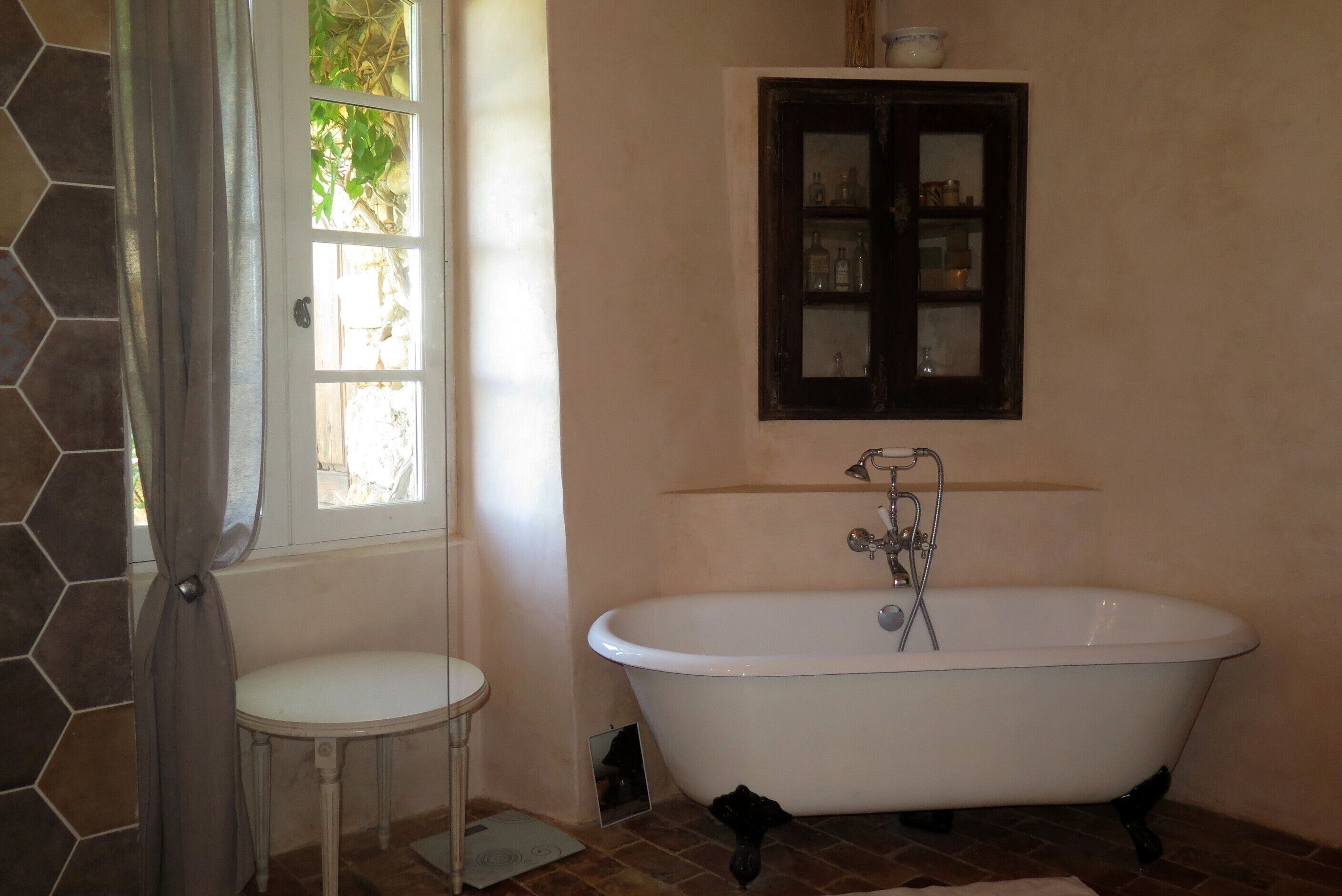 Un bagno con una vasca freestanding, un lavandino piccolo e rotondo, e un pensile sopra la vasca.