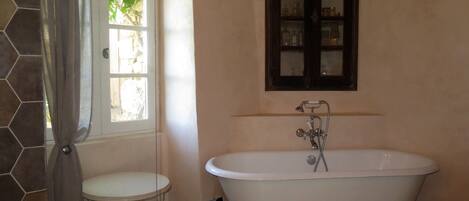Un bagno con una vasca freestanding, un lavandino piccolo e rotondo, e un pensile sopra la vasca.