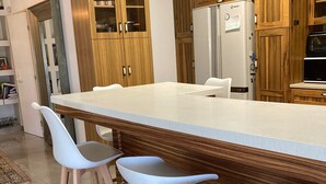 A modern kitchen with a large island, wooden cabinets, and white bar stools. - Pardes Villa (Pardes Hanna-Karkur)