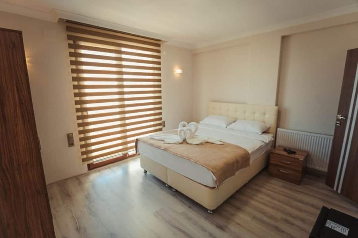 Quarto com cama, piso de madeira, radiador e porta de madeira.