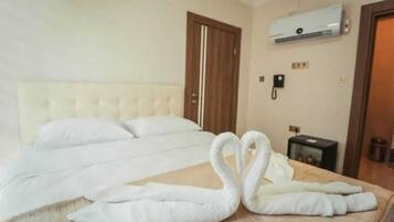 Habitación de hotel con una cama grande, una puerta de madera, un aire acondicionado, un teléfono y una mesita pequeña.