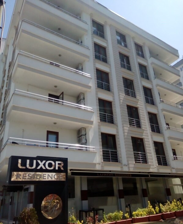 A multi-story building with balconies, a sign for 'LUXOR RESIDENCE', and a circular window. - Luxor Residance (Akçaabat)