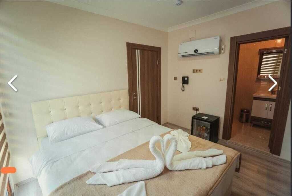 A hotel room with a large bed, a bedside table, an air conditioning unit, and a bathroom visible through an open door.