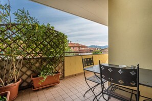 Un balcon avec une table et des chaises, des plantes en pot et une vue sur les bâtiments en arrière-plan.