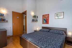 Une chambre à coucher comprenant un lit, des tables de chevet, une armoire, un radiateur et des étagères avec des livres et des objets décoratifs.