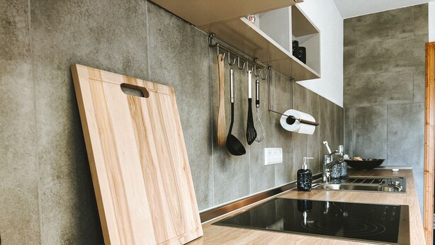 Une cuisine moderne avec un plan de travail en bois, une plaque de cuisson noire et des ustensiles suspendus.