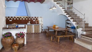 A spacious kitchen with a wooden table and benches, a staircase with a railing, and a view of the sky. - Ca la Partida (San Rafael del Río)
