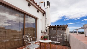 A patio with two metal chairs and a small round table, a potted plant, and a view of the cityscape. - Ca la Partida (San Rafael del Río)