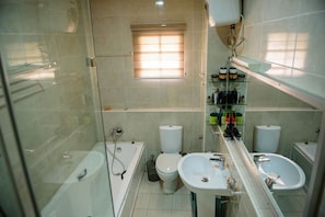 A modern bathroom with a glass shower enclosure, two toilets, a sink, and a vanity with toiletries. - Beautiful 4-bedroom House Located in Abuja (Abuja)