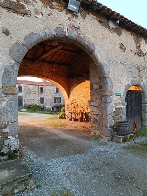 An arched stone structure with a rustic wooden ceiling, a sign indicating 'Chambres d'Hotes', and a barrel outside.