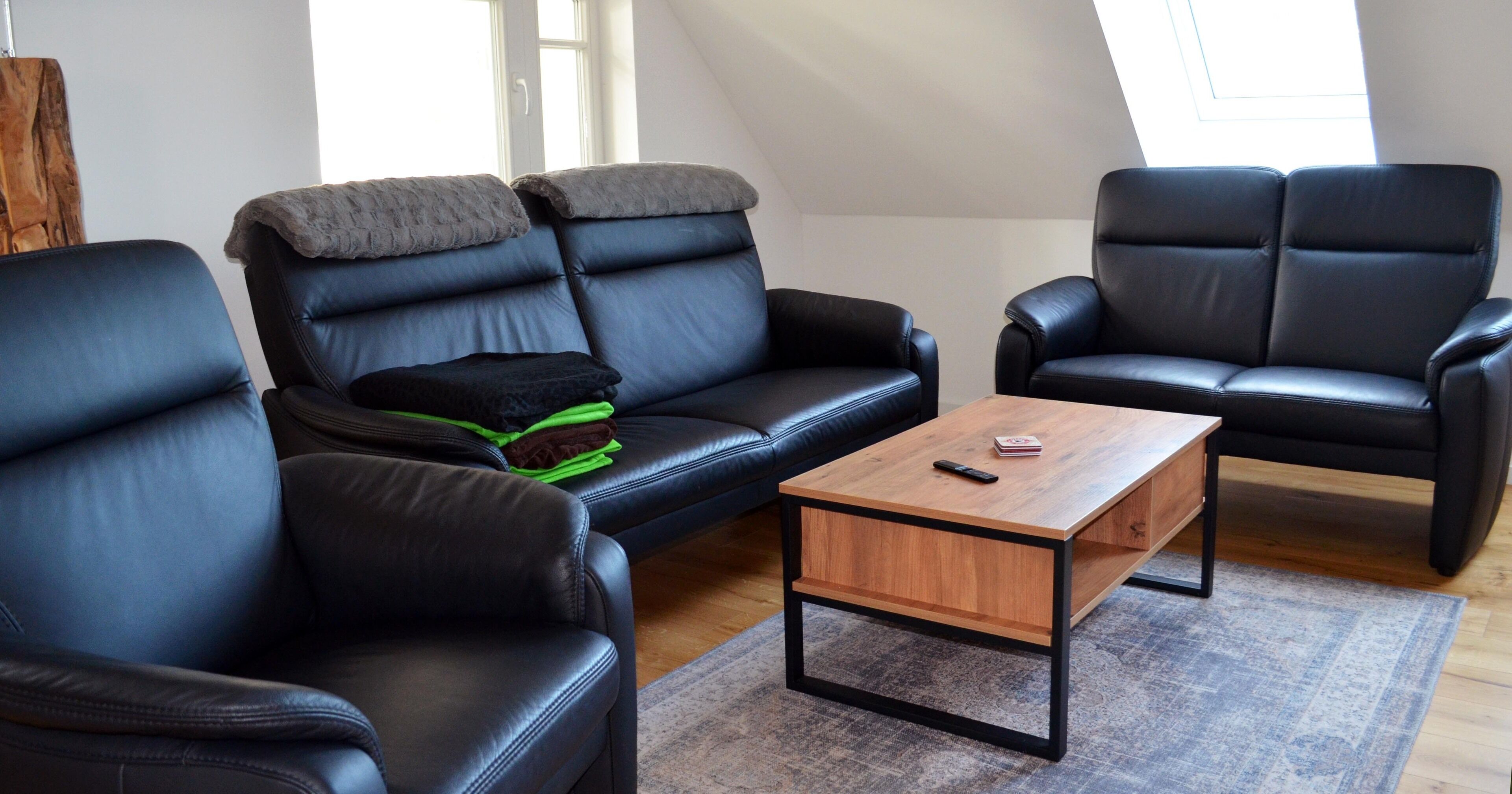A modern living room with a black leather sofa, a matching armchair, and a wooden coffee table.