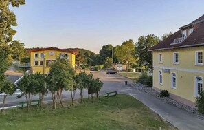 Un bâtiment jaune avec un toit rouge, une route pavée et un banc au premier plan.