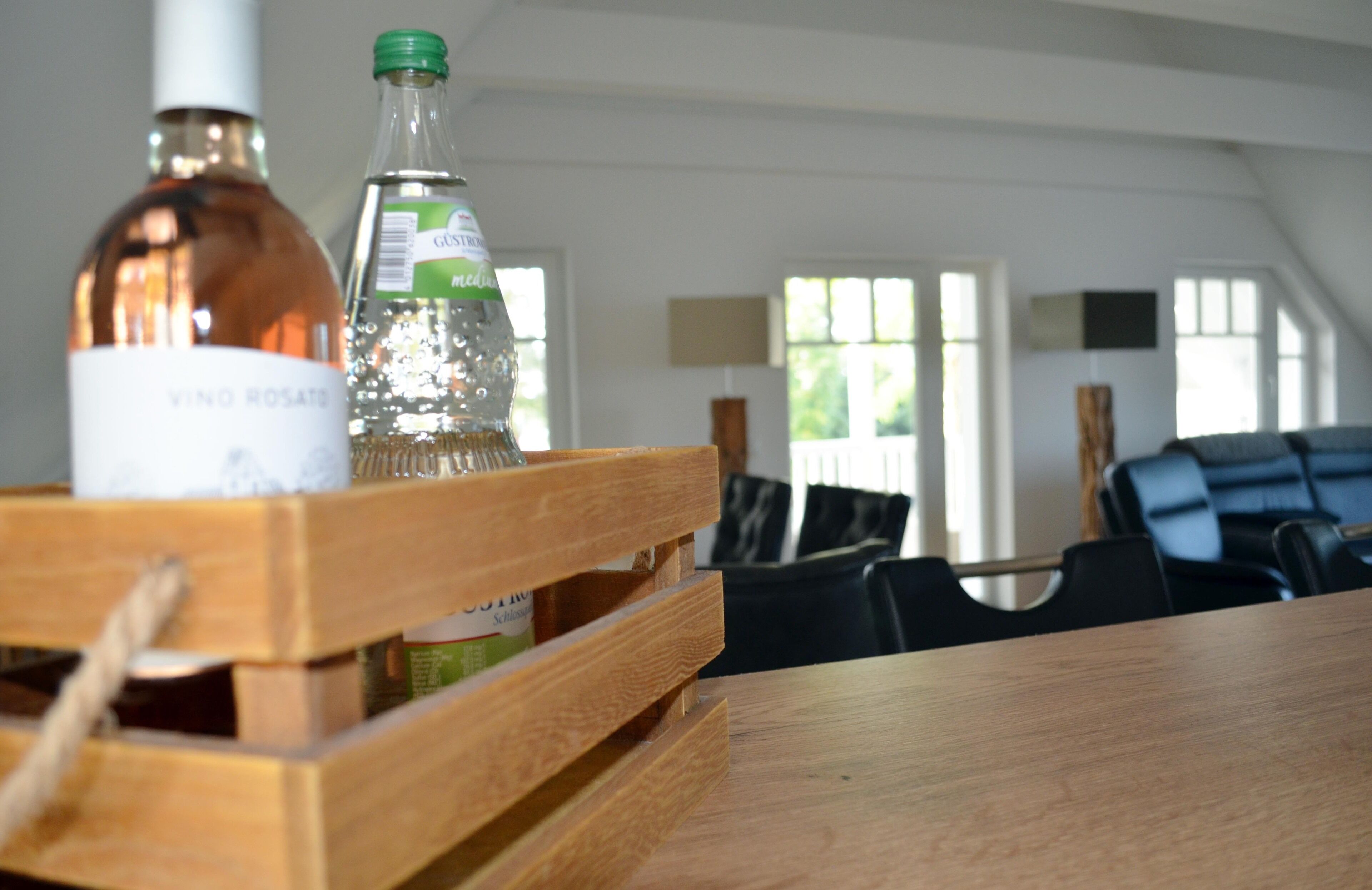 Una caja de madera con botellas sobre una mesa en una habitación con techos altos y ventanas amplias.