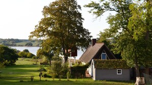 Ein Haus mit einem strohgedeckten Dach, umgeben von üppiger Vegetation und einem See im Hintergrund.