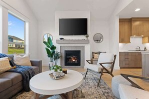Un salon moderne doté d’une cheminée, d’un téléviseur à écran plat et d’un coin cuisine avec des meubles en bois.