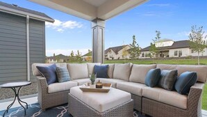 Ein überdachter Patio-Bereich mit einer Eckcouch, einem kleinen Tisch und einer dekorativen Ablagefläche.