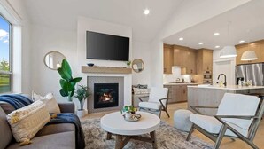 Ein modernes Wohnzimmer mit Kamin, Sofa, Couchtisch und Küchenzeile mit Holzschränken und einem Edelstahlkühlschrank.