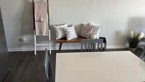 Una habitación con una escalera de madera apoyada en una pared, un banco con cojines y una planta en maceta.