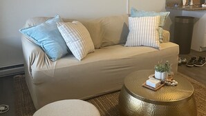 Una sala de estar con un sofá color beige, una mesa redonda de centro y un pequeño reposapiés.