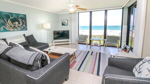 A living room with a sofa, TV, and a view of the beach.