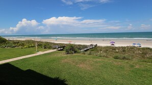 A beach with a wooden walkway leading to the shore, a few umbrellas, and a clear view of the ocean.