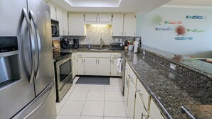 A modern kitchen with a stainless steel refrigerator, built-in oven, and granite countertop.