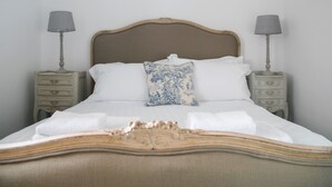 Ein Bett mit Holz-Kopfstück, weißer Bettwäsche und einem Zierkissen. Es gibt zwei Nachttische mit Lampen und eine kleine Schublade.