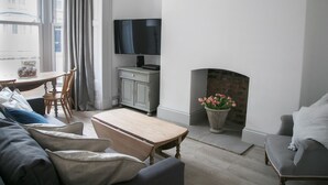 Ein Wohnzimmer mit Kamin, Fernseher, Esstisch mit Stühlen und einer Couch.