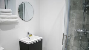 Ein modernes Badezimmer mit einem weißen Waschbecken, einem schwarzen Schrank und einer Duschkabine aus Glas.