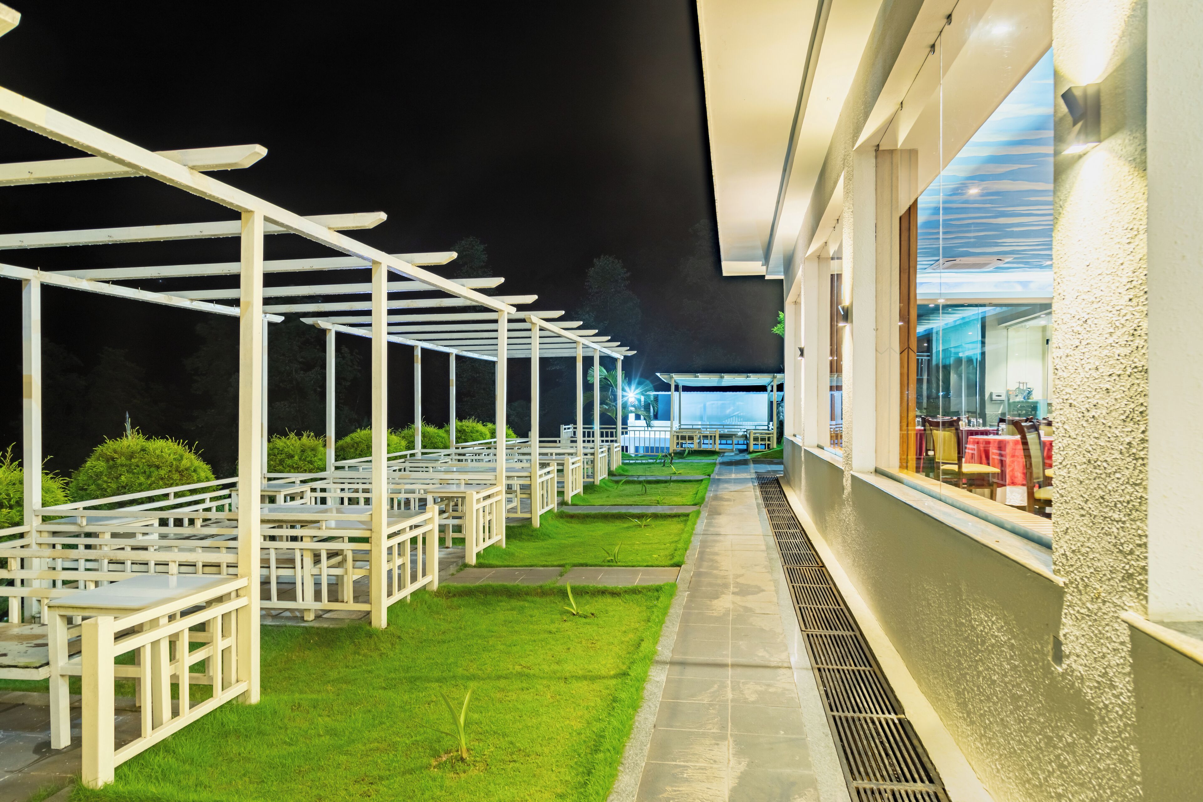 An outdoor seating area with white tables and chairs, a grassy lawn, and a building with a glass facade.