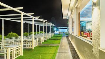 An outdoor seating area with white tables and chairs, a grassy lawn, and a building with a glass facade.