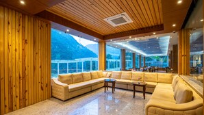 A spacious living area with a large sectional sofa, a coffee table, and a view of a mountainous landscape through large windows. - Bhotekoshi Heli Resort and Spa (Marming)