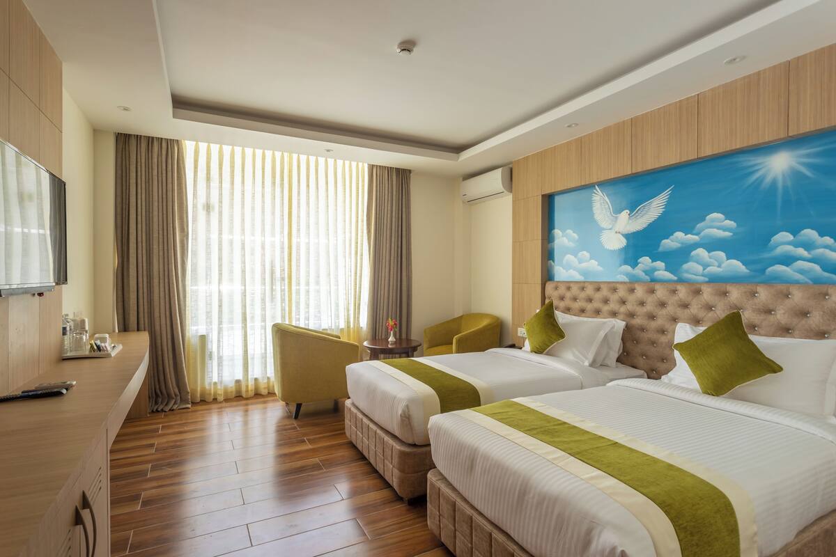 Una habitación de hotel con dos camas, televisión, escritorio y ventana con cortinas.